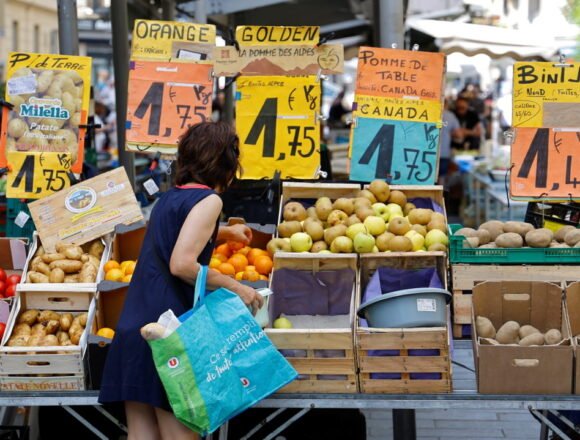Price tags are seen as a woman shops at a local market in Nice التضخم