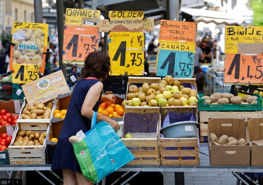 Price tags are seen as a woman shops at a local market in Nice التضخم